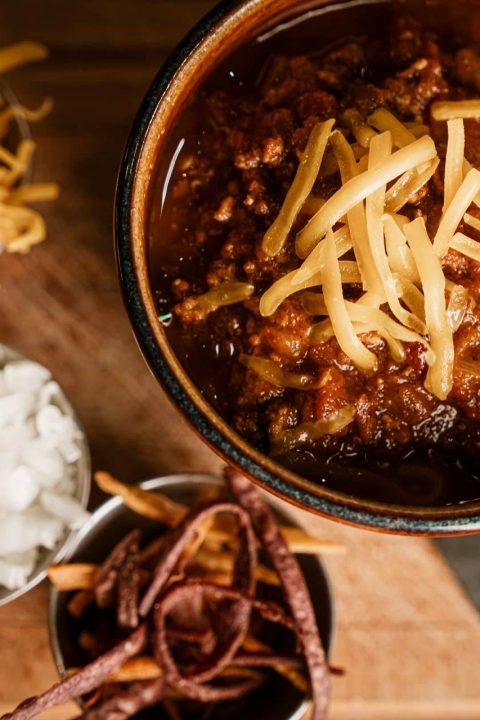 Bowl of house chili topped with cheddar, onions, and tortilla strips