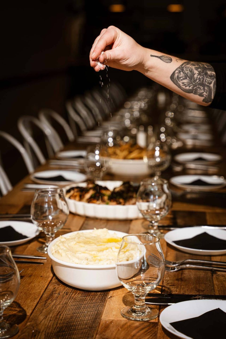 Chef seasoning a family-style dinner spread